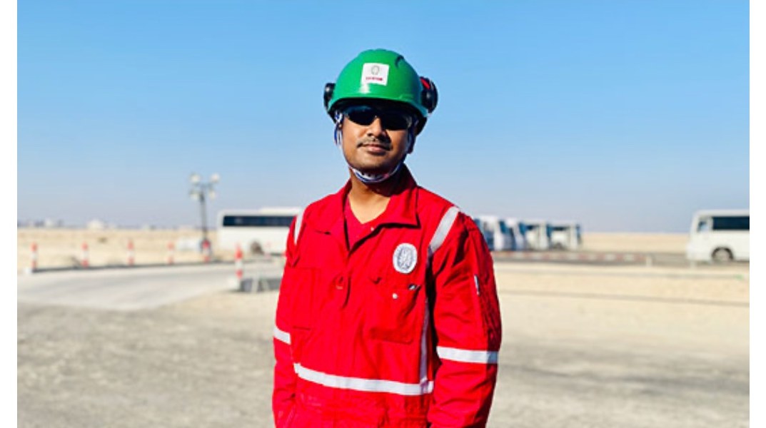 Ram on site in Qatar, wearing a green hard hat and red coveralls